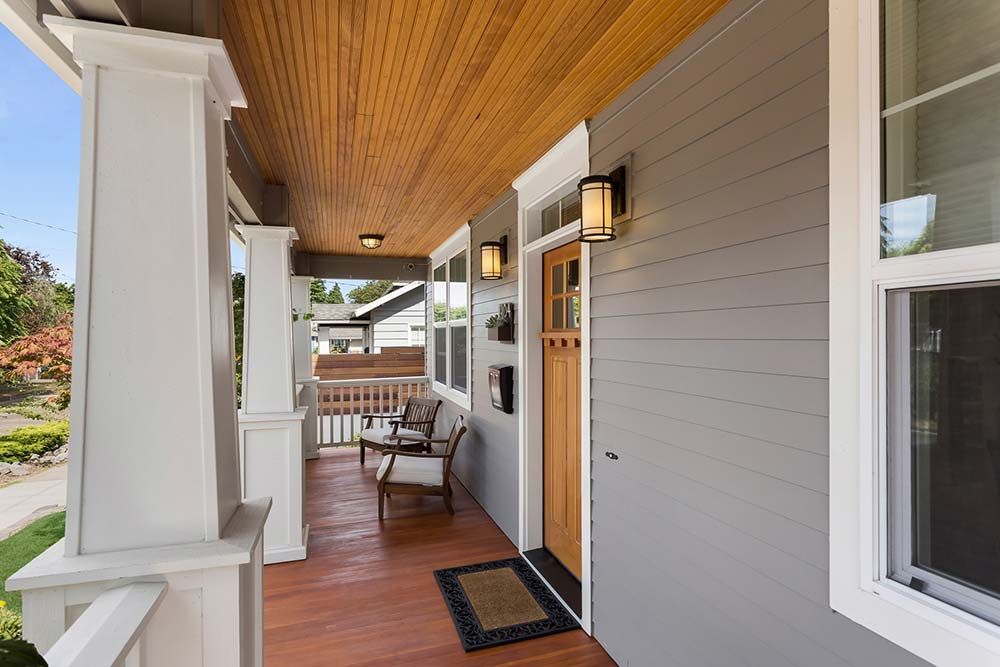 The front porch of a house with a wooden ceiling and a bench.