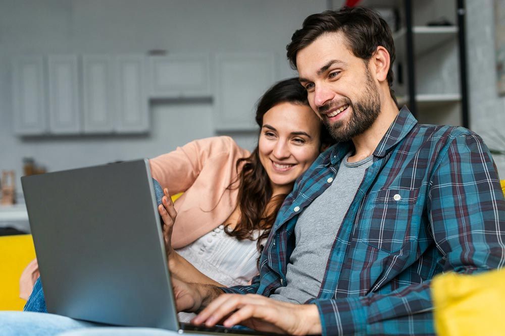 A man and a woman are sitting on a couch using a laptop computer.