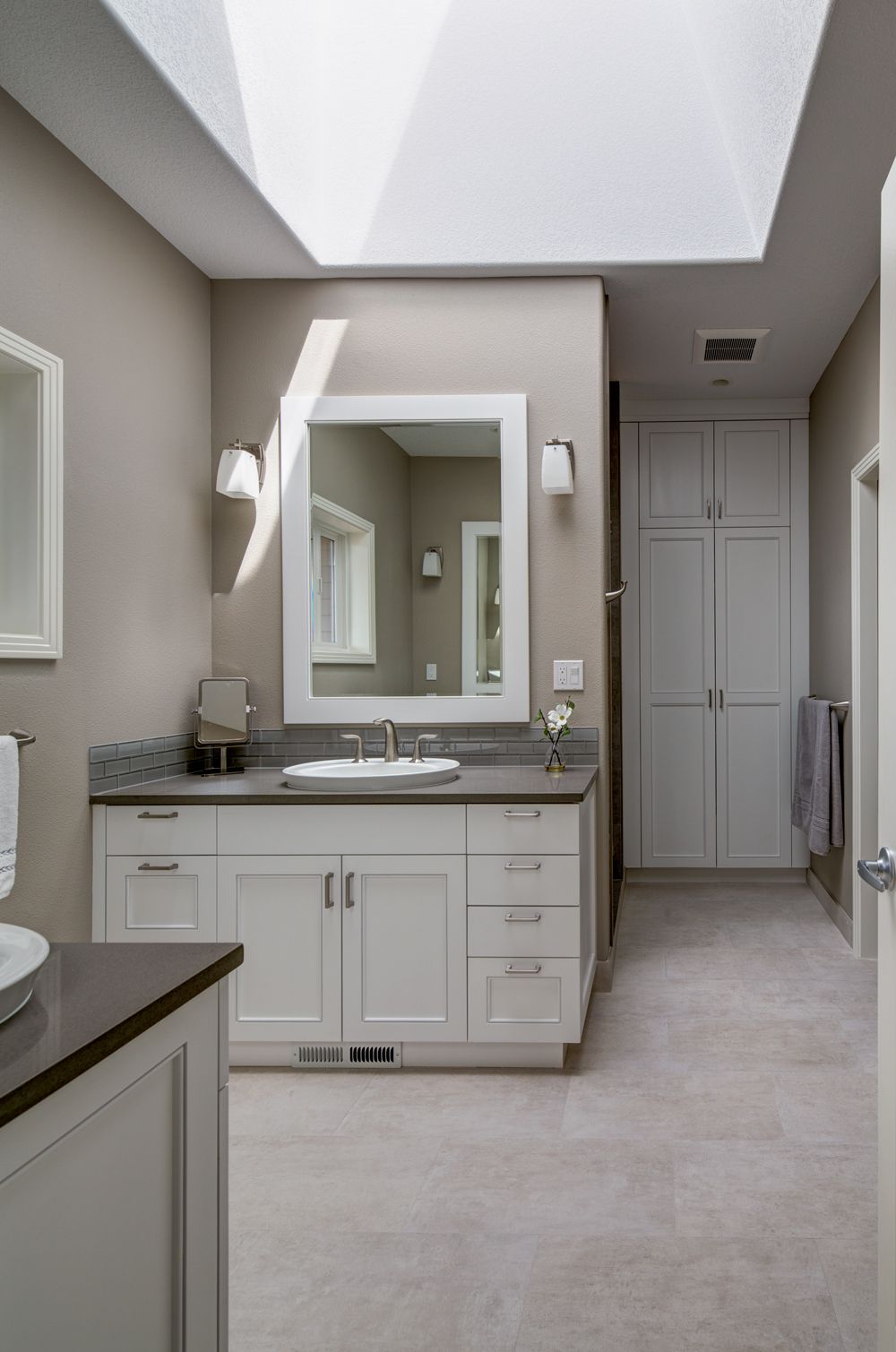 A bathroom with a skylight above the sink and mirror