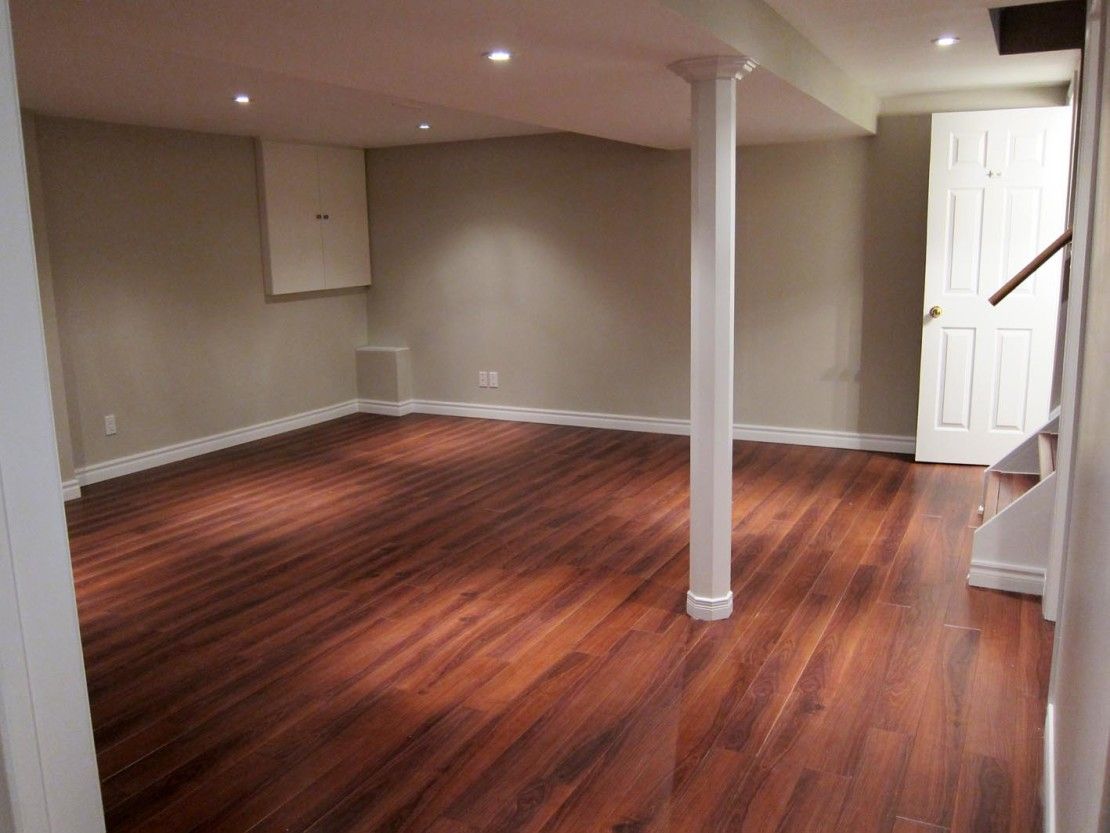 An empty basement with hardwood floors and a white door