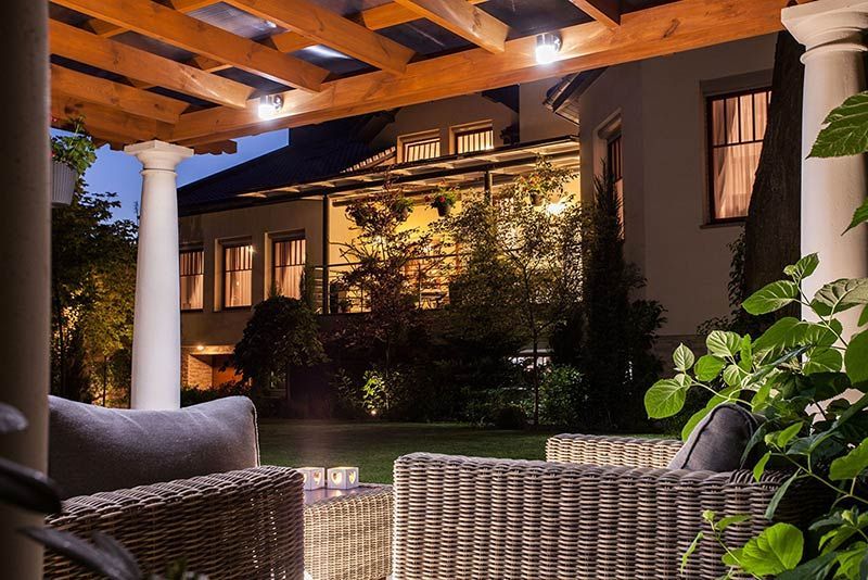 A patio with wicker furniture and a pergola at night.