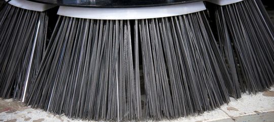 Black bristles of a street sweeper brush with a metal rim, shown close up.