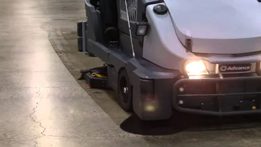Automated floor-cleaning machine with headlights on, moving along a polished indoor floor