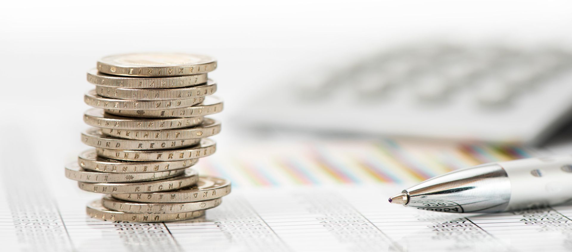 Stack of coins with a pen, calculator and financial chart background.