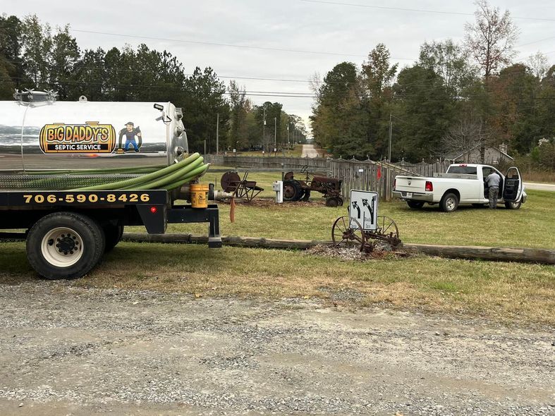 A tanker truck is parked in a gravel lot next to a white truck.
