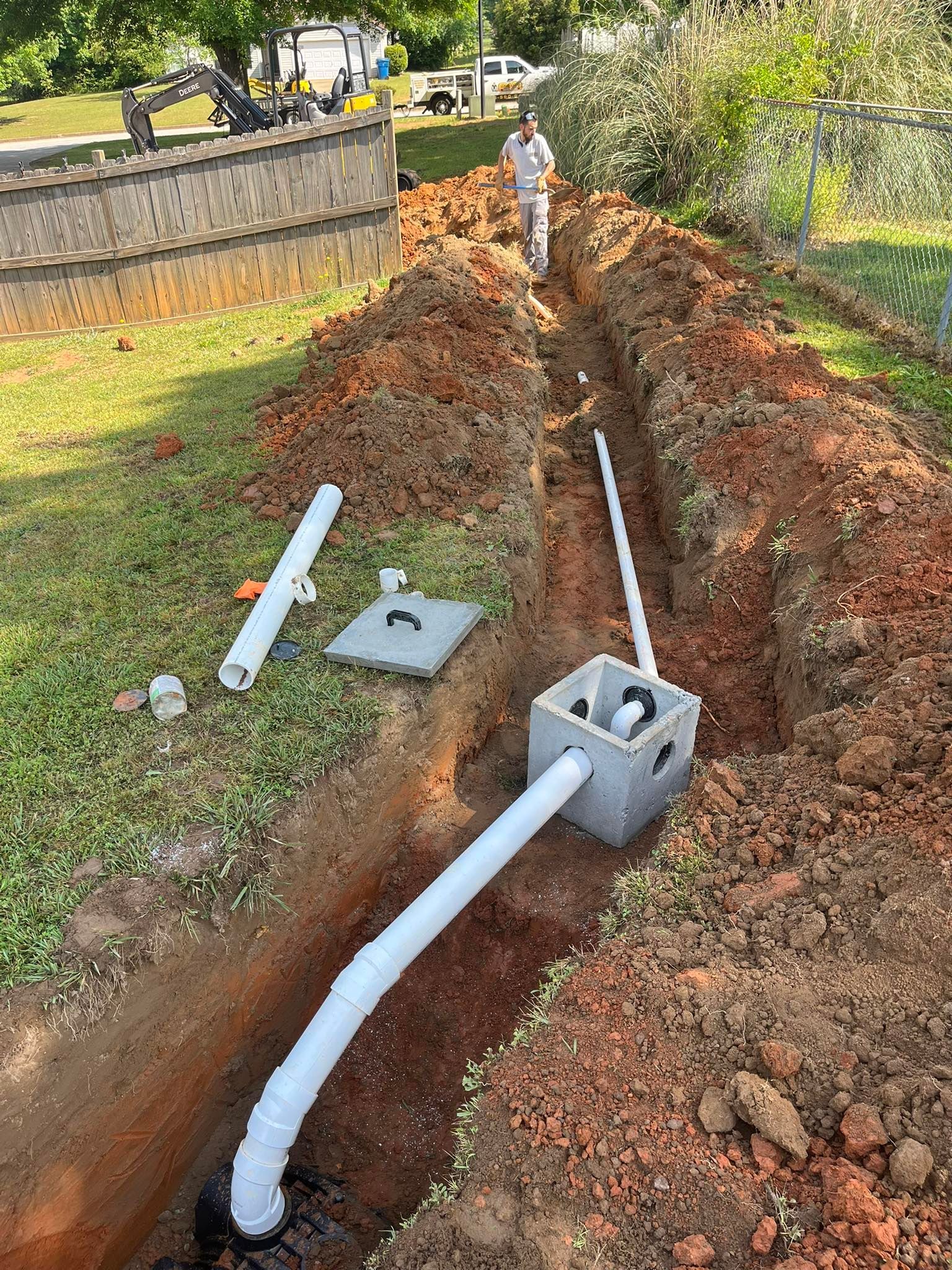 A man is using a yellow excavator to dig a hole in the ground.