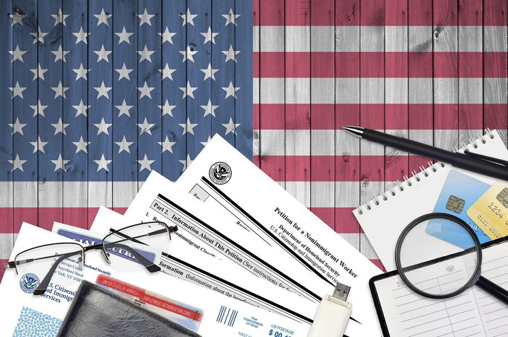 A magnifying glass, glasses, and office supplies atop official documents on a background of the United States flag.