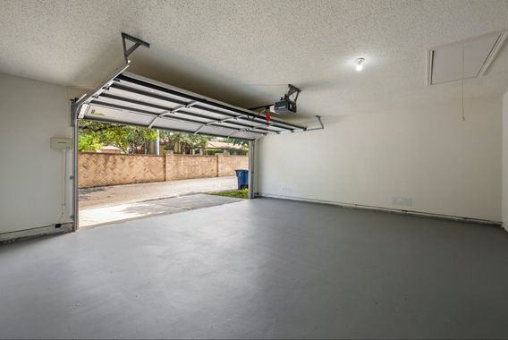 Empty garage with gray floor, open door, white walls, and a visible driveway.