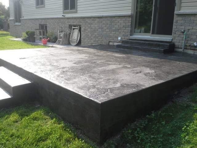 Concrete patio with steps, next to a house with brick siding, on a grassy lawn.