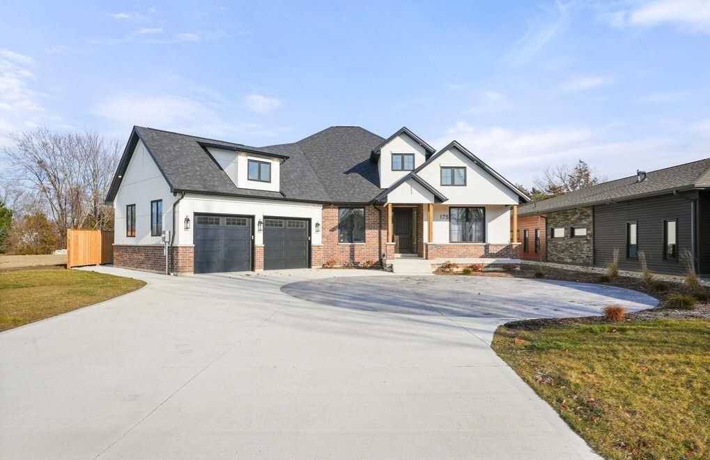 Modern two-story house with black roof, brick facade, and concrete driveway on a sunny day.
