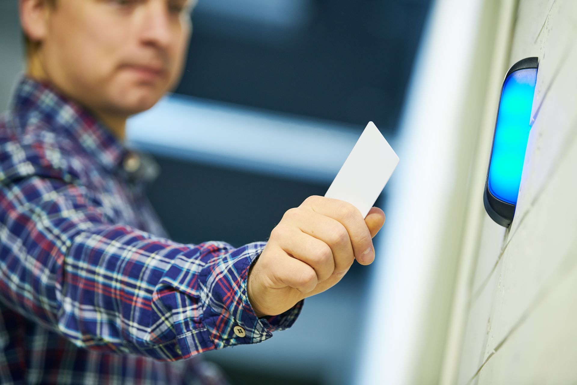 Man in plaid shirt using a card to access a blue-lit security reader. Man in plaid shirt using a card to access a blue-lit security reader.