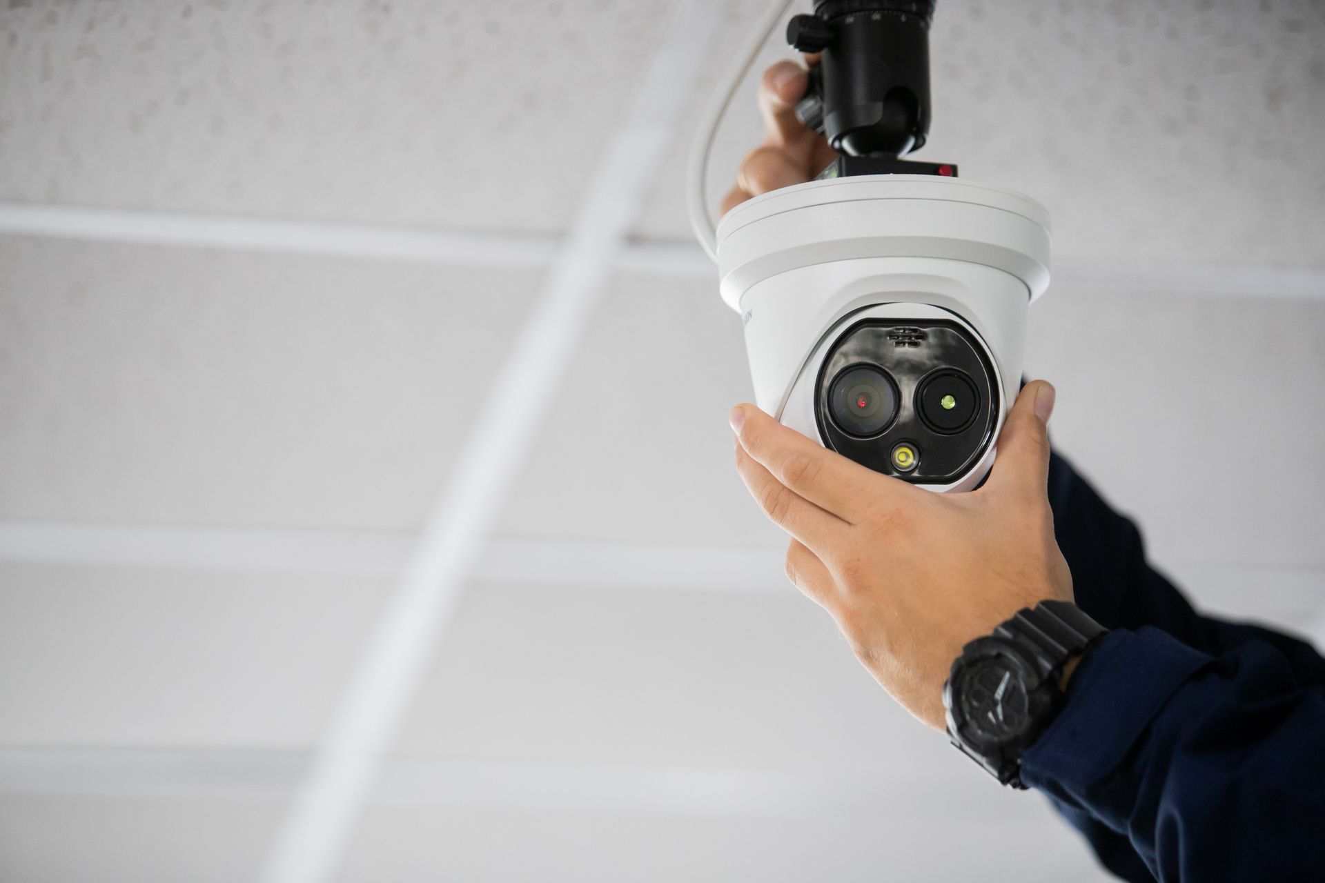 A security system installer is mounting a surveillance camera on the ceiling.