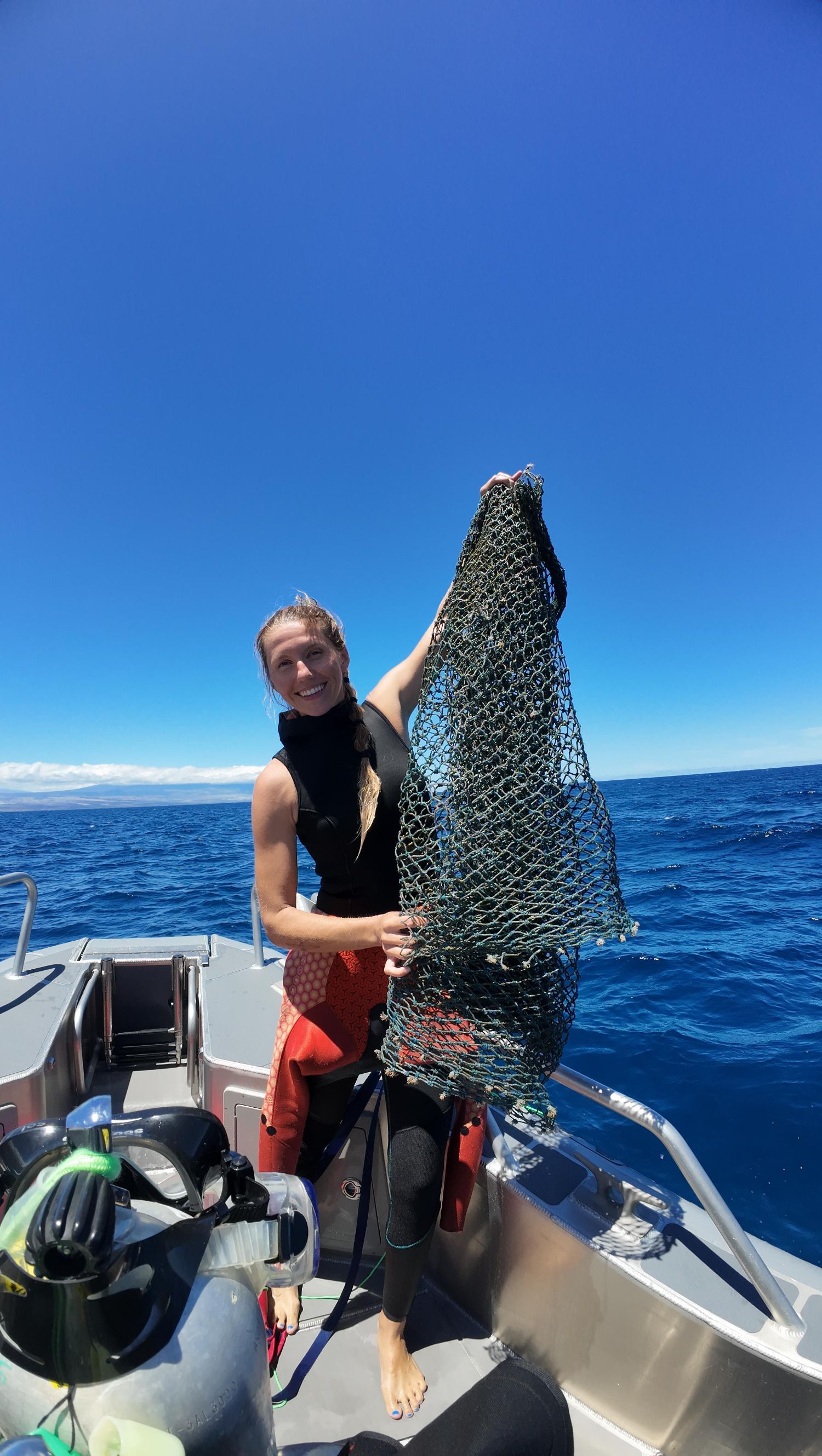 A woman is holding a fishing net on a boat in the ocean.