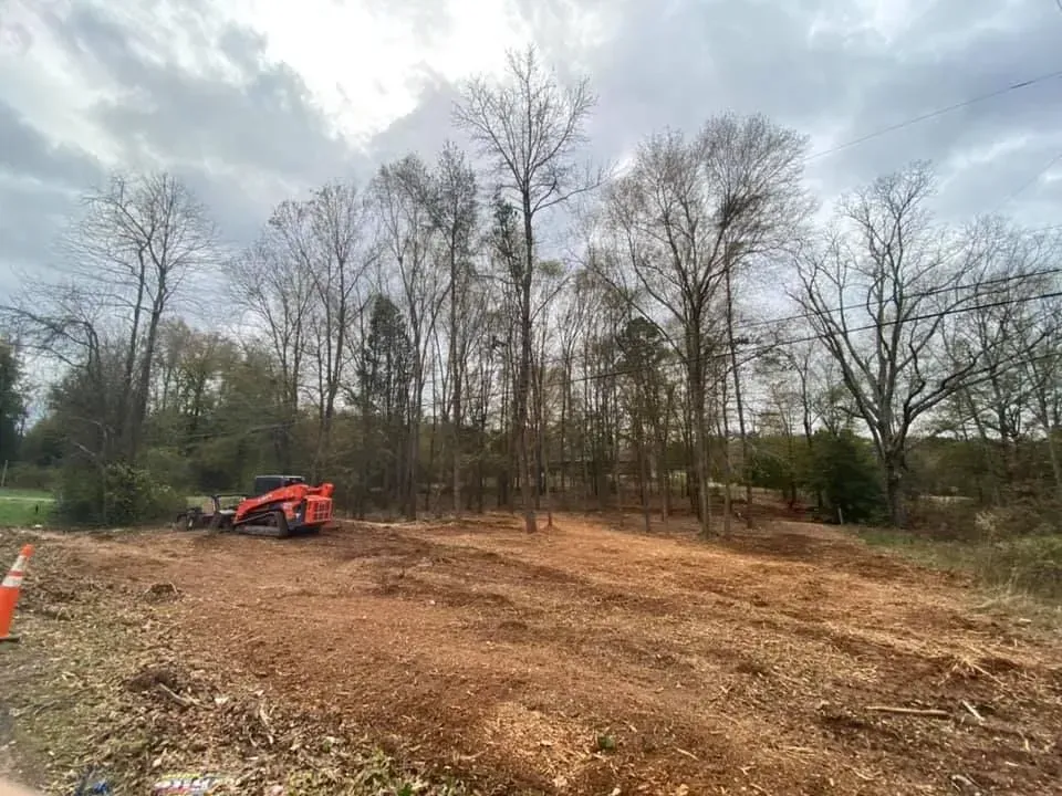A large dirt field with trees in the background and a bulldozer in the foreground.