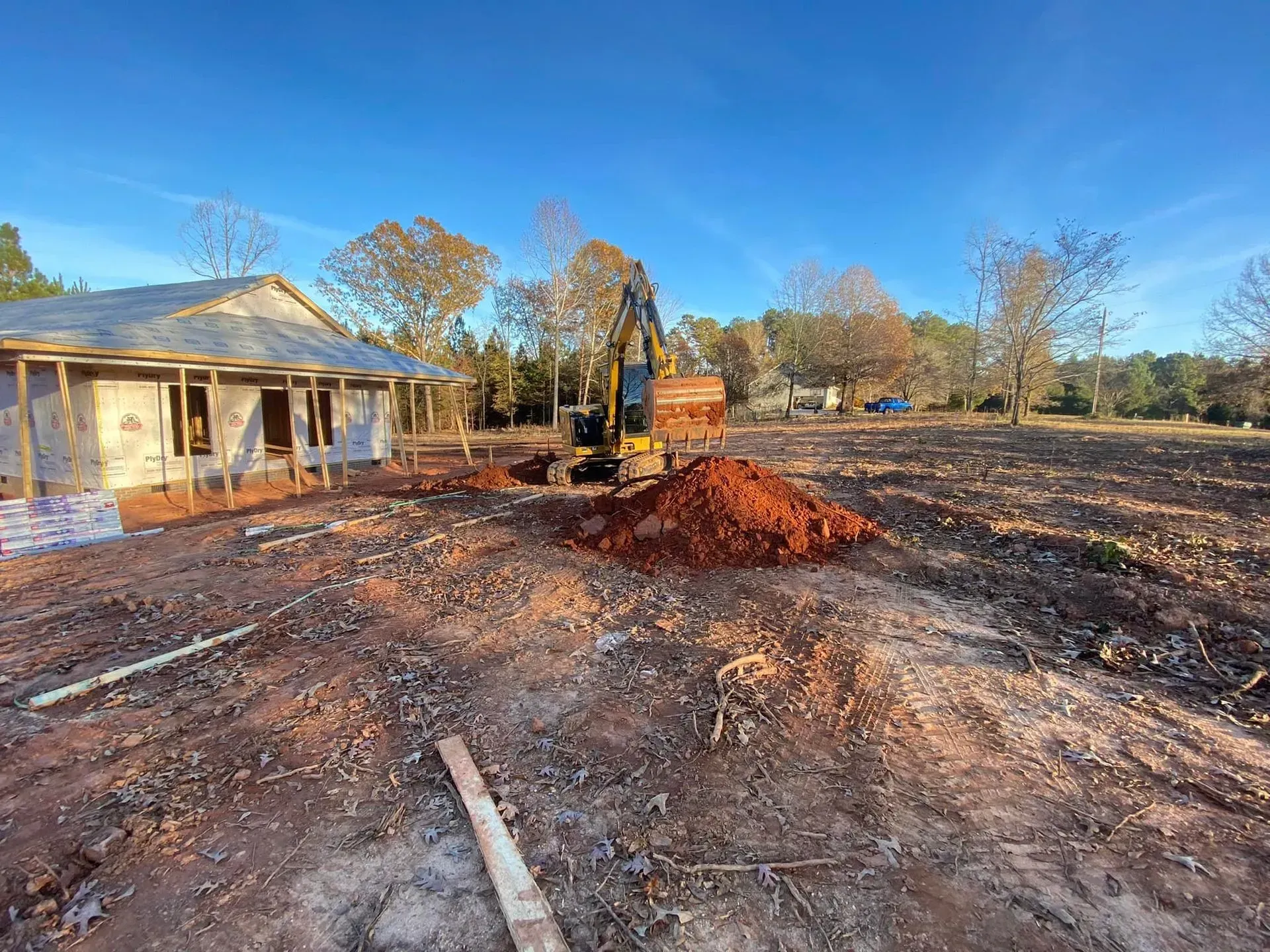 A bulldozer is digging a hole in the dirt in front of a house under construction.