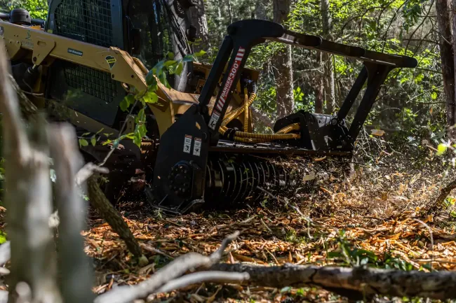 A tractor is cutting trees in the woods.
