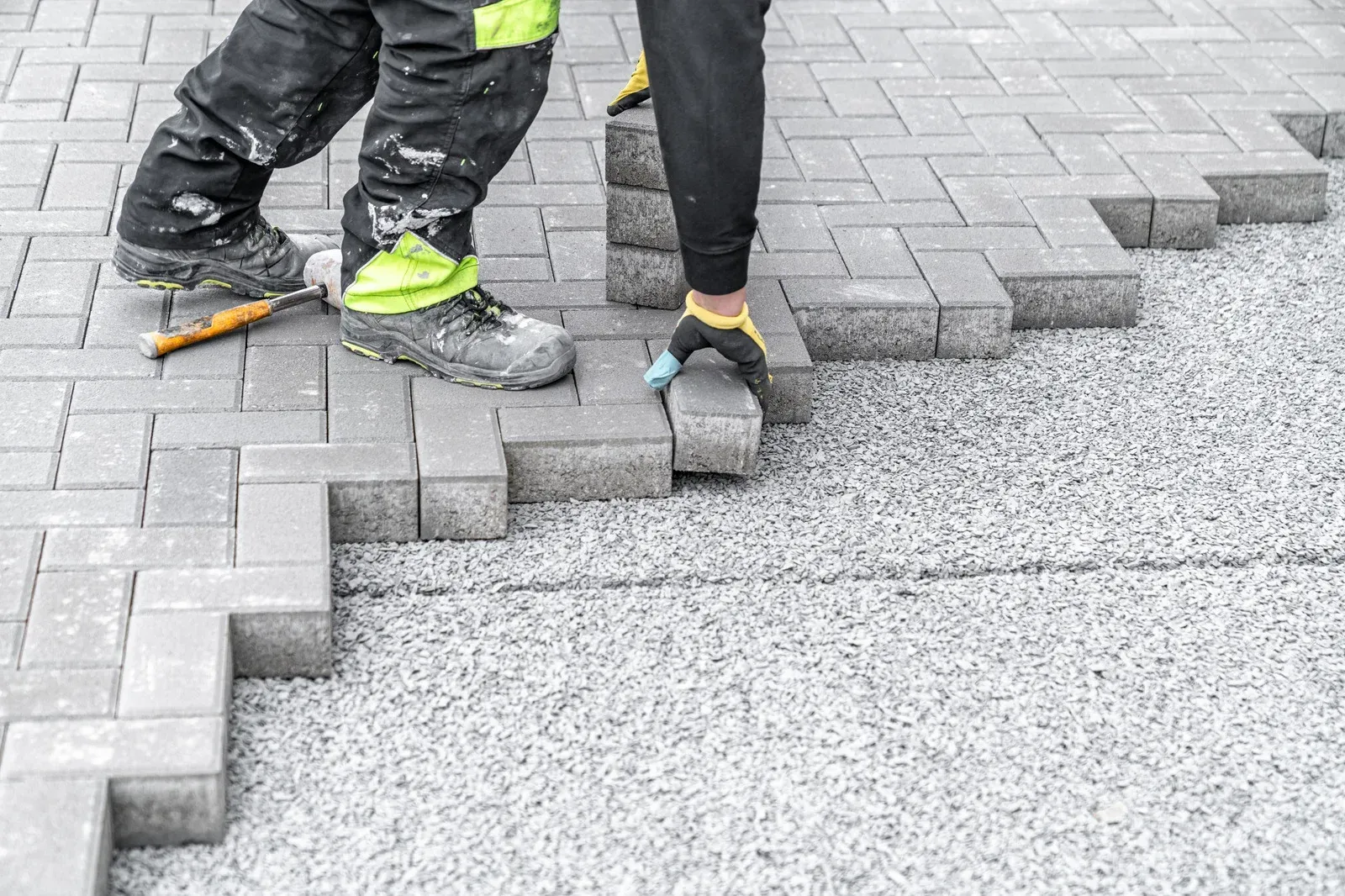 Person laying gray paving stones on gravel base.