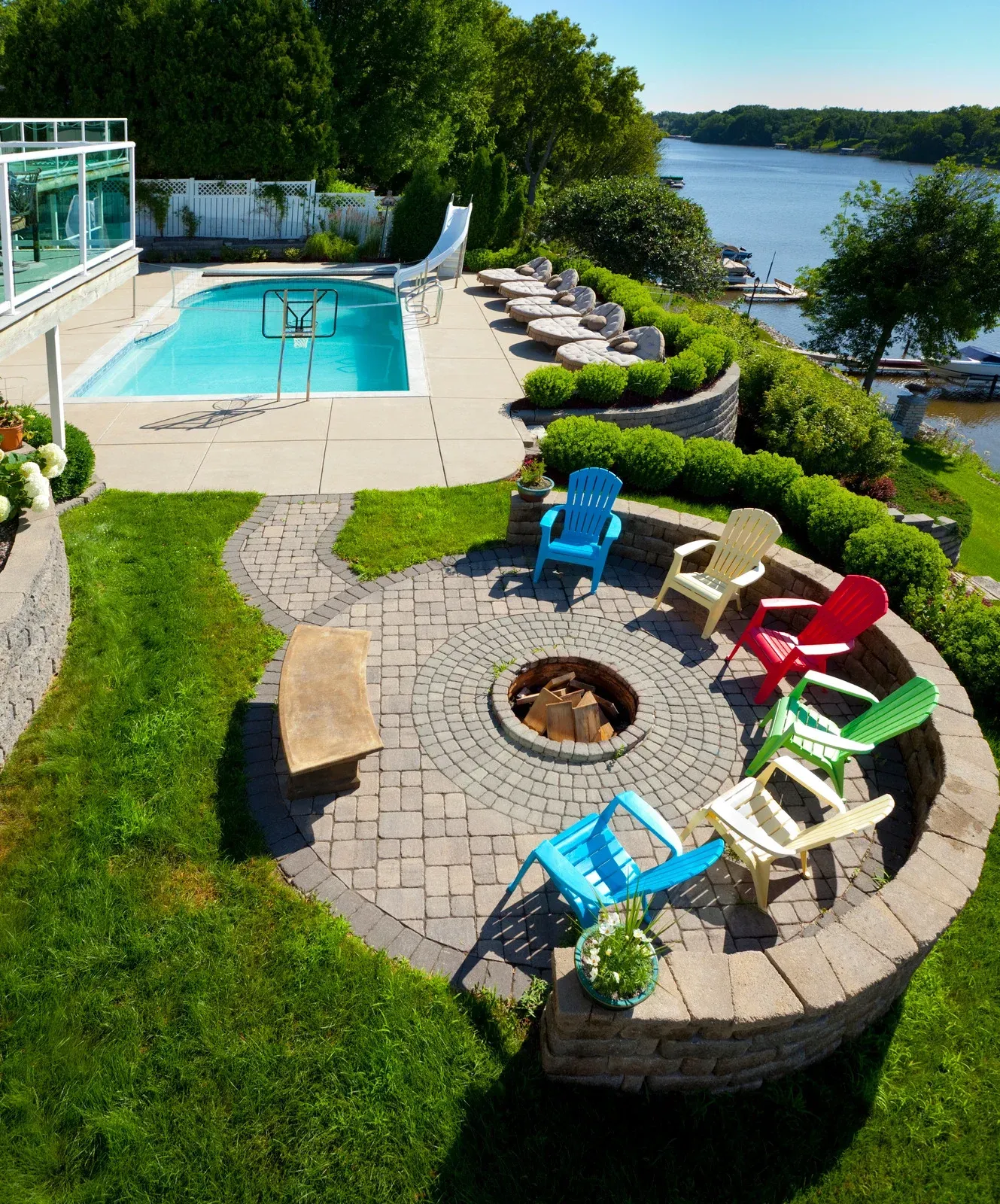 Pool and fire pit area overlooking a river. Colorful Adirondack chairs surround a fire pit.