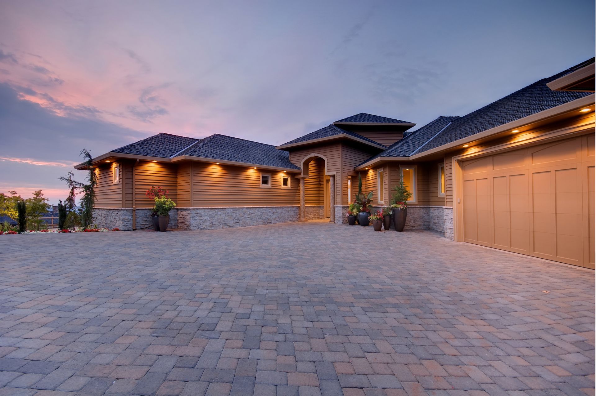 Elegant wood and stone home with arched entryway and paved driveway at dusk.