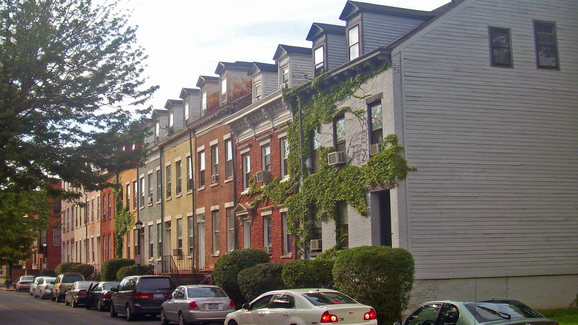 Two-story house with blue siding and a gray roof. Dusk setting with lit windows and a teal front door.