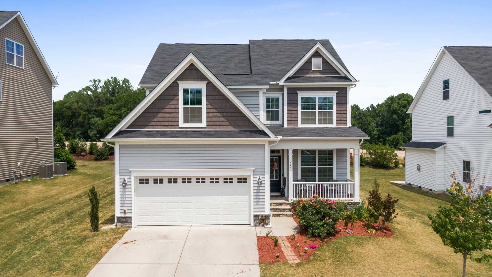 Two-story house with gray siding, brown accents, and a white garage door, blue sky in the background.