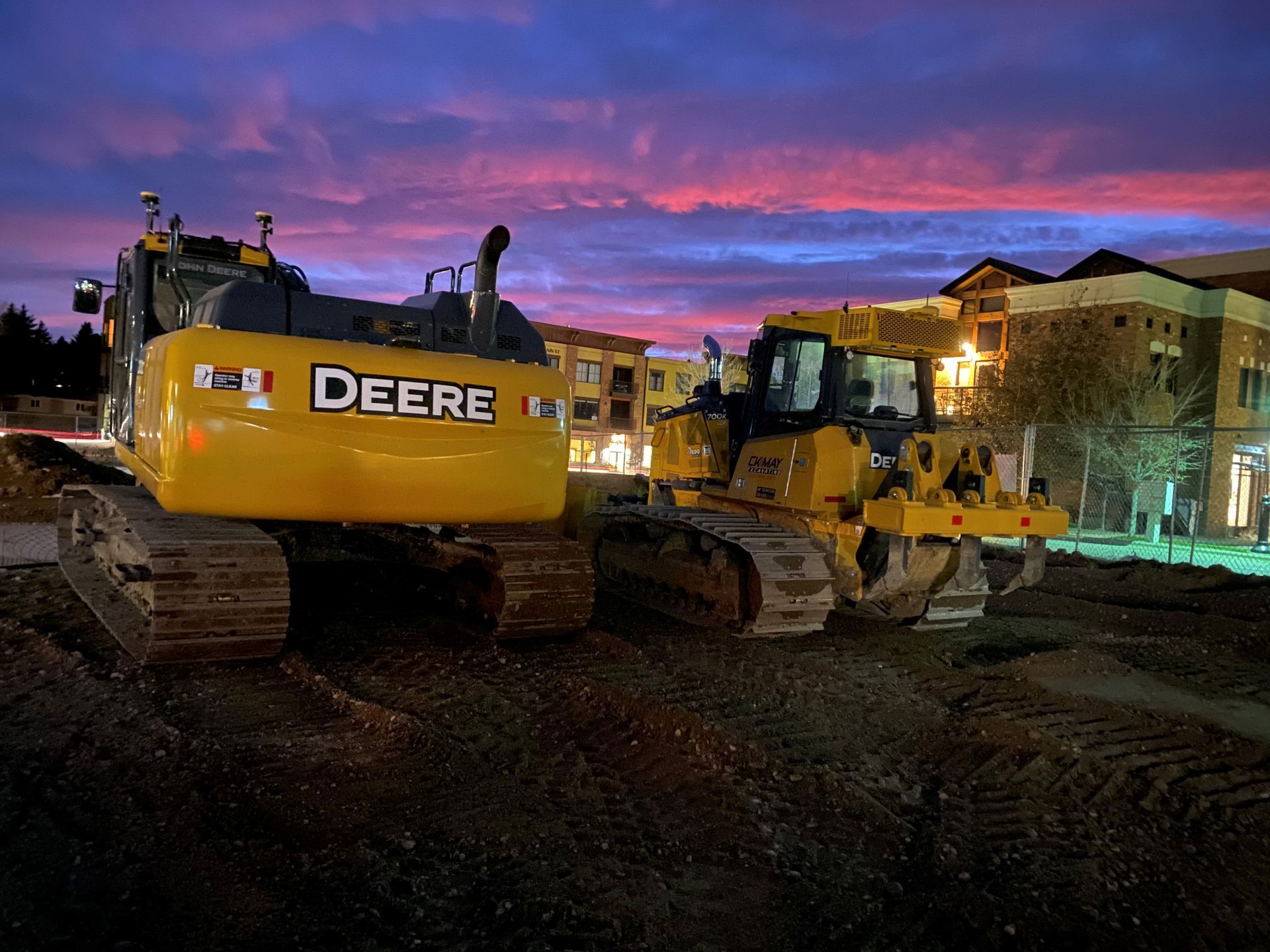 Two deere bulldozers are parked on a construction site at night.