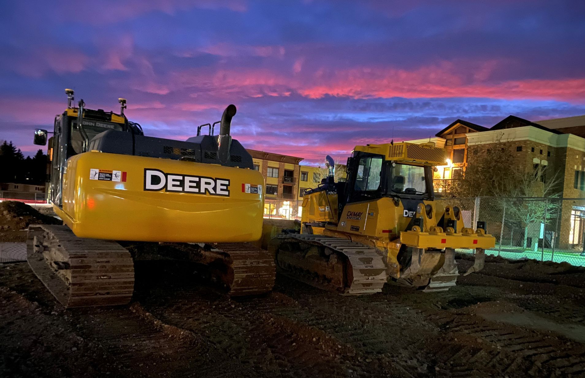 Two deere bulldozers are parked on a construction site at night.