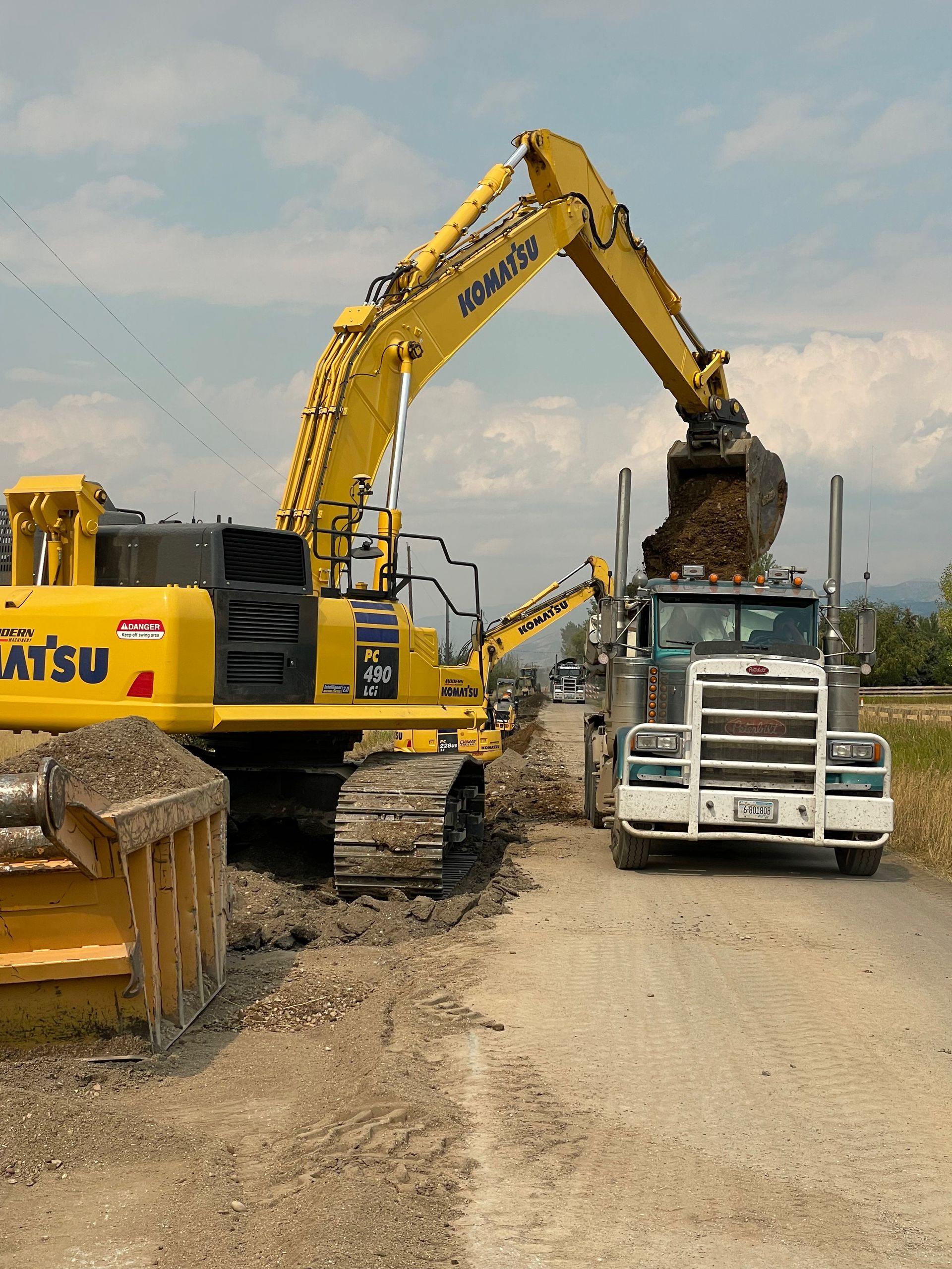 A yellow komatsu excavator is loading dirt into a truck