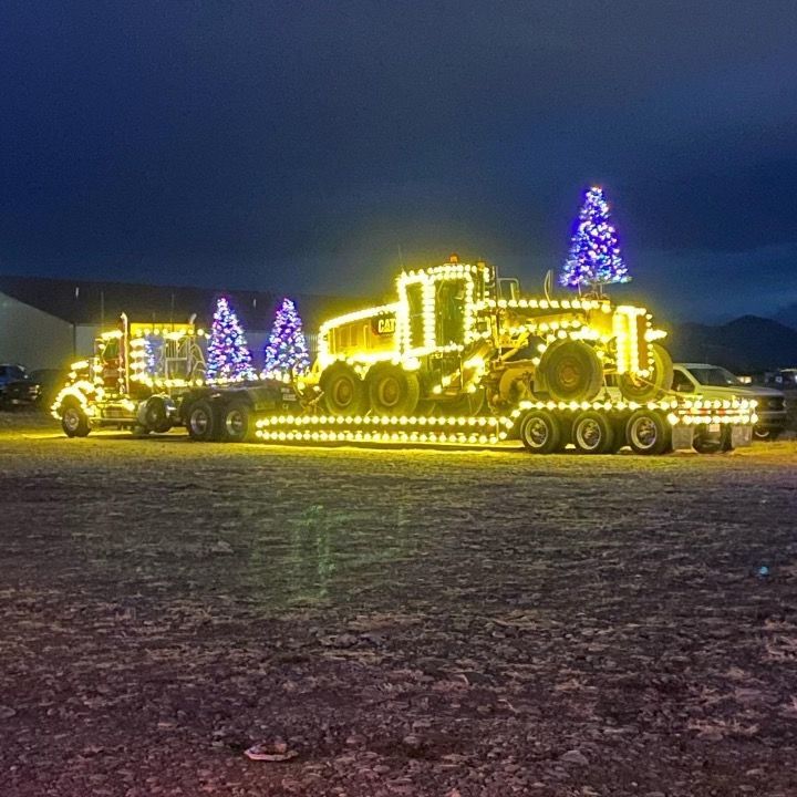 A truck with a tractor on the back is decorated with christmas lights.
