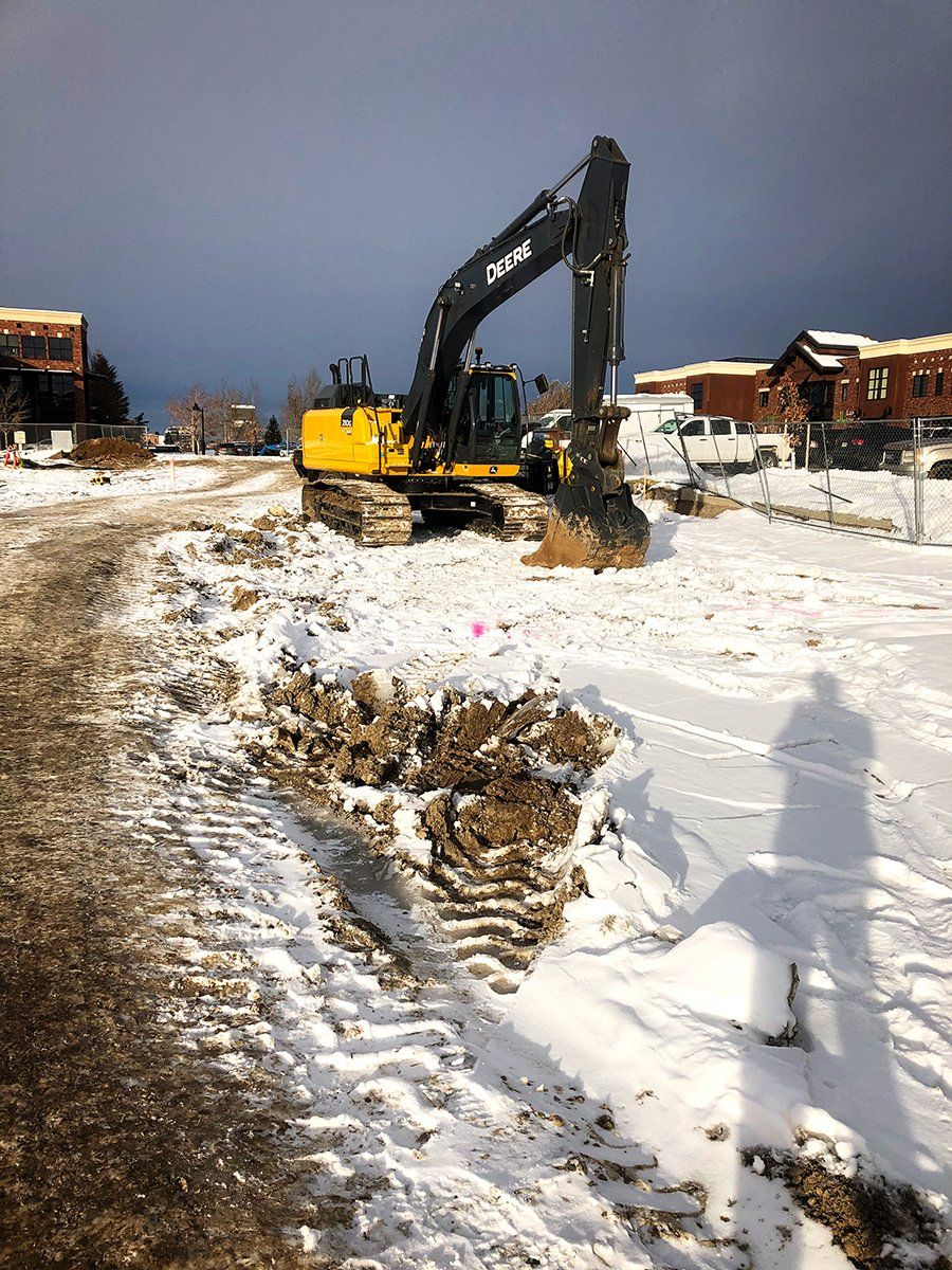 A yellow excavator is digging a hole in the snow.