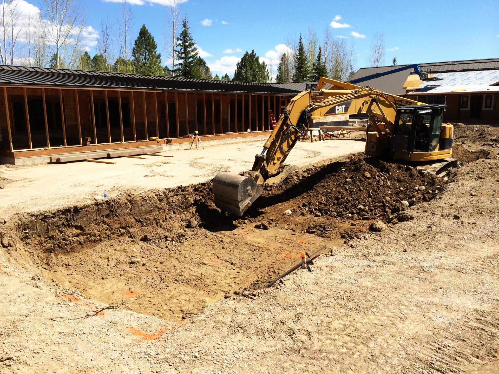 An excavator is digging a hole in the dirt in front of a building under construction.