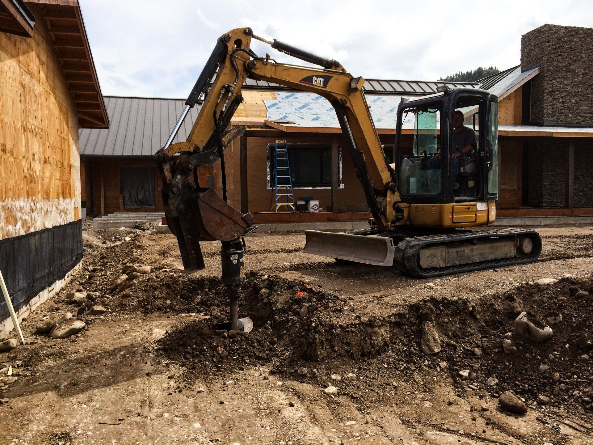 An excavator is digging a hole in the dirt in front of a house under construction.