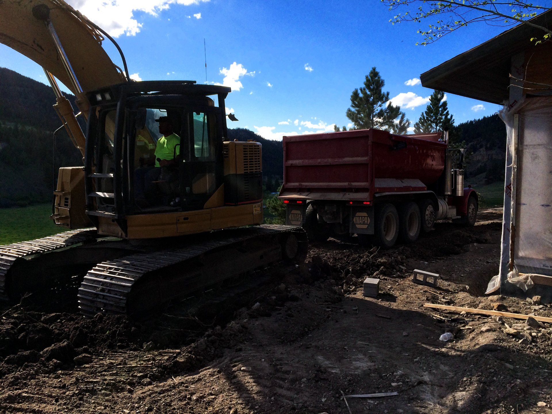 A bulldozer is pulling a red dump truck on a dirt road
