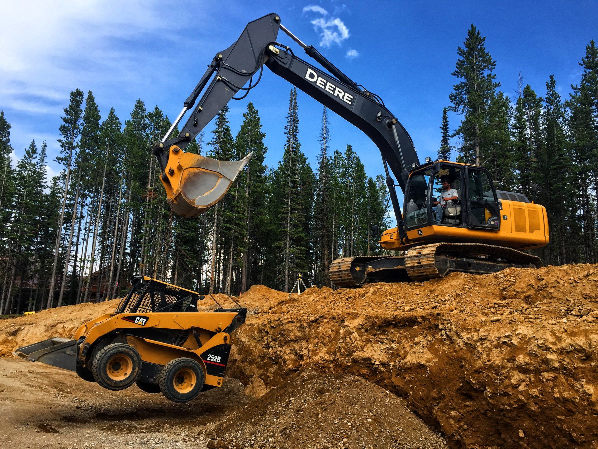 A deere excavator is loading dirt into a skid steer loader.