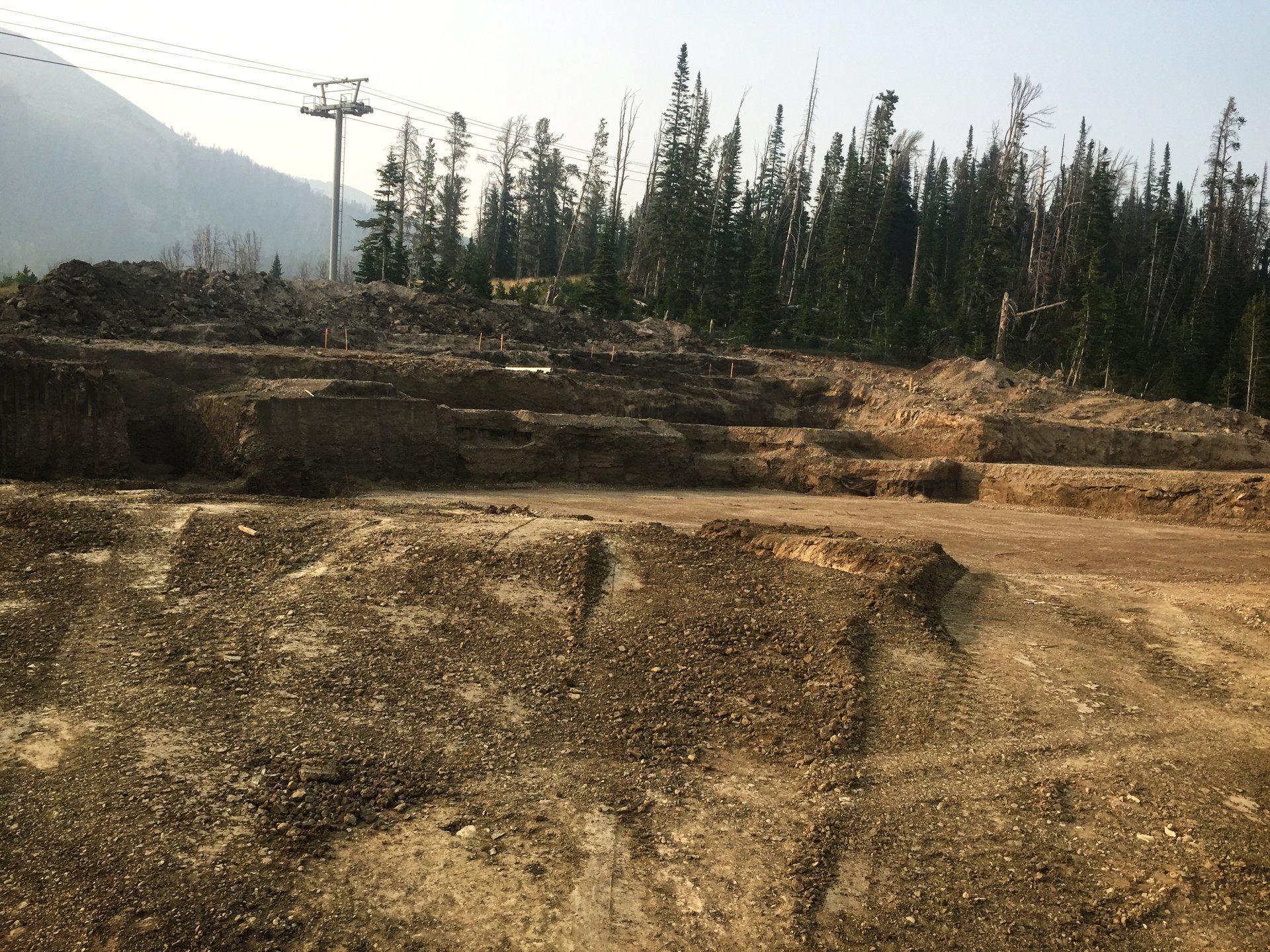 A dirt field with trees in the background and a ski lift in the background.