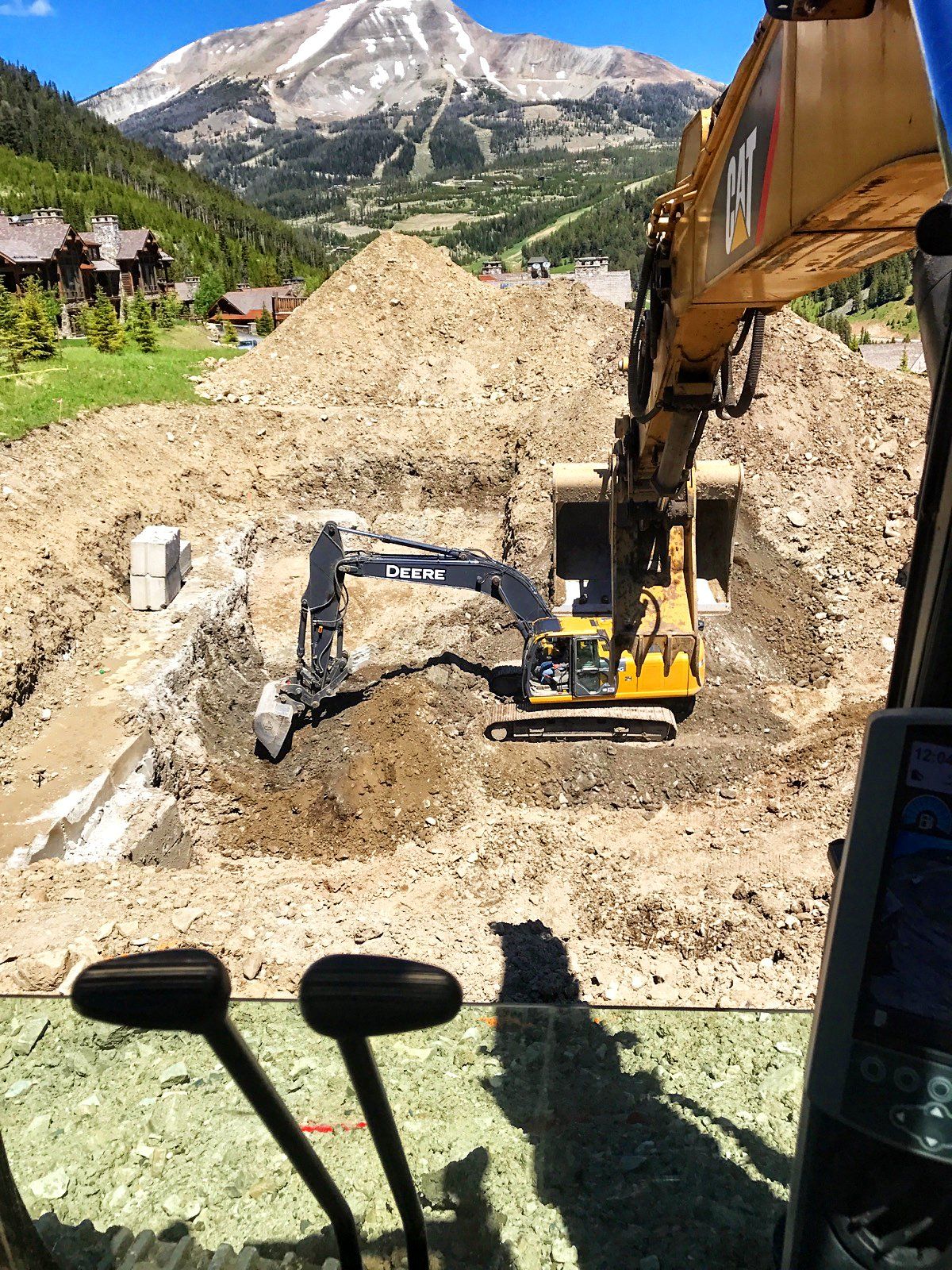 A yellow excavator is digging a hole in the dirt with a mountain in the background.
