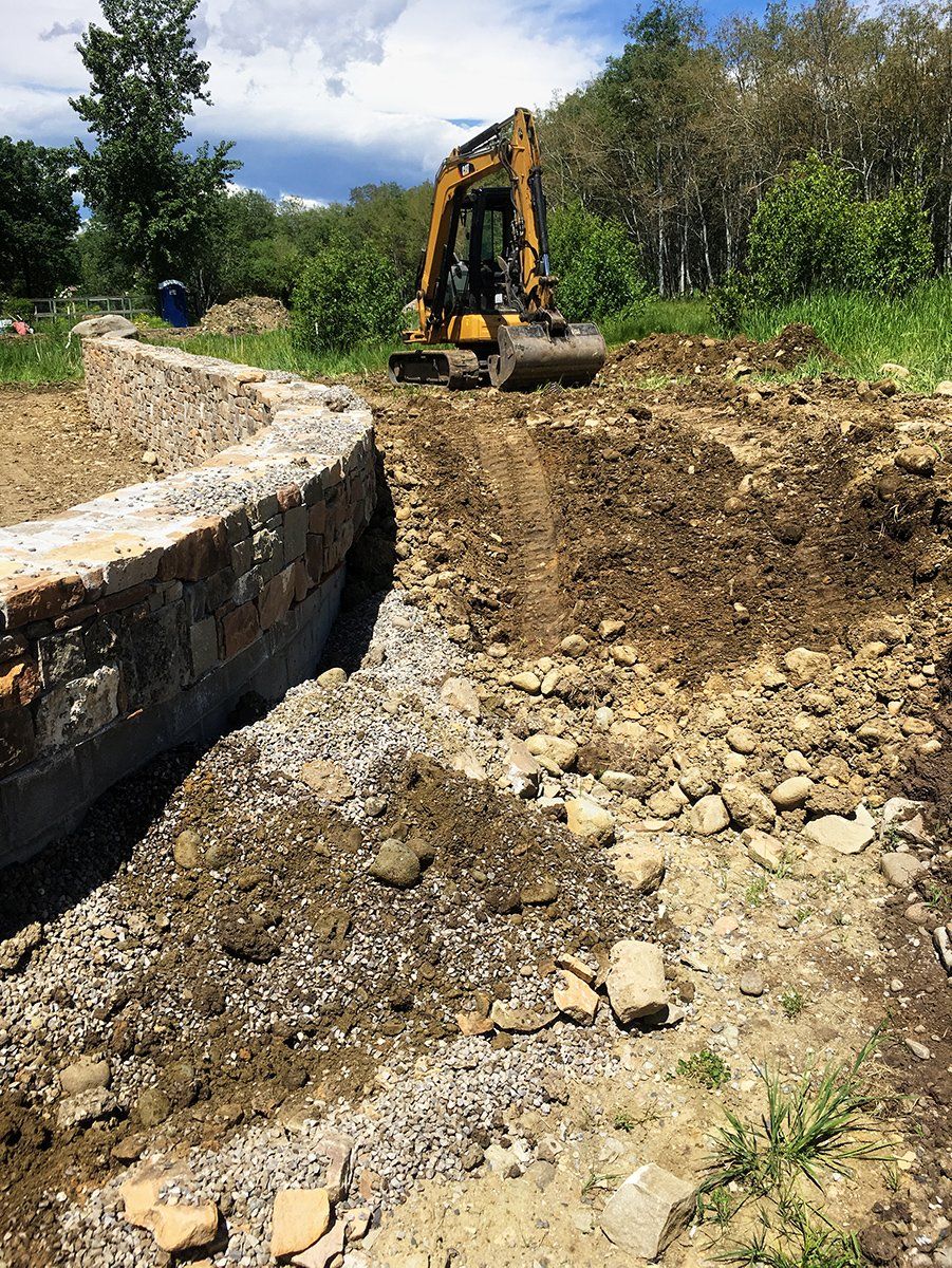 A bulldozer is moving dirt in a field next to a stone wall.
