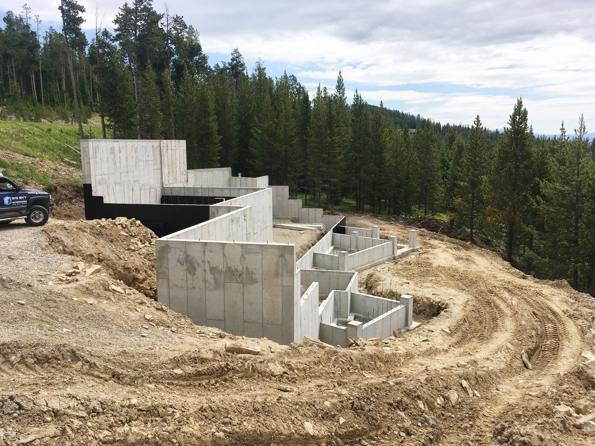 A house is being built on top of a dirt hill surrounded by trees.