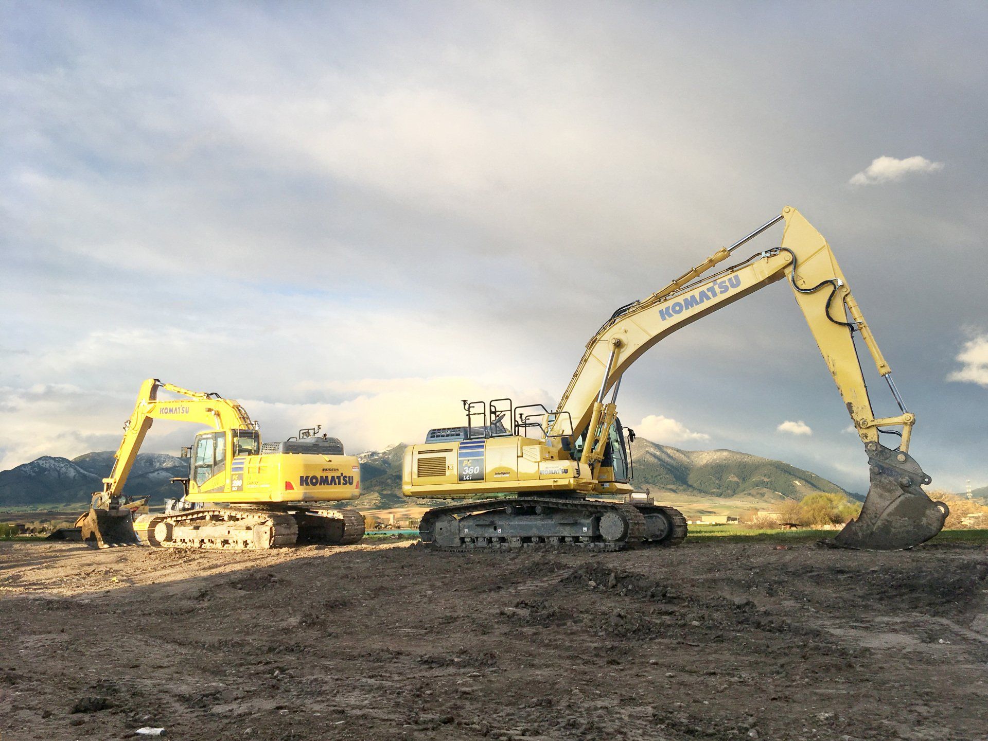 Two large yellow excavators are sitting on top of a dirt field.