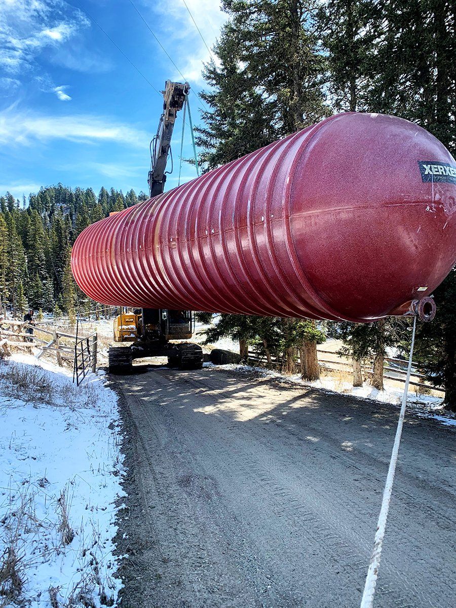 A large red tank is being lifted by a crane down a snowy road.