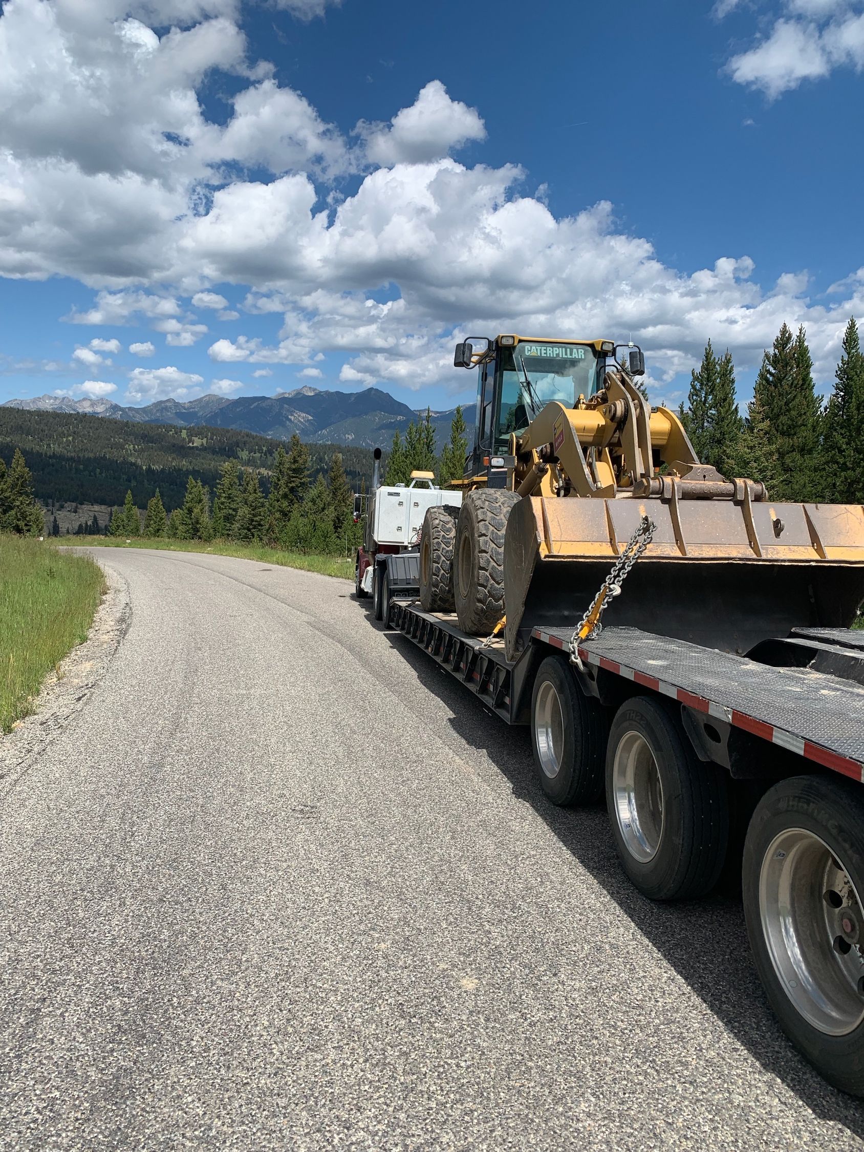 A bulldozer is sitting on top of a trailer on a gravel road.
