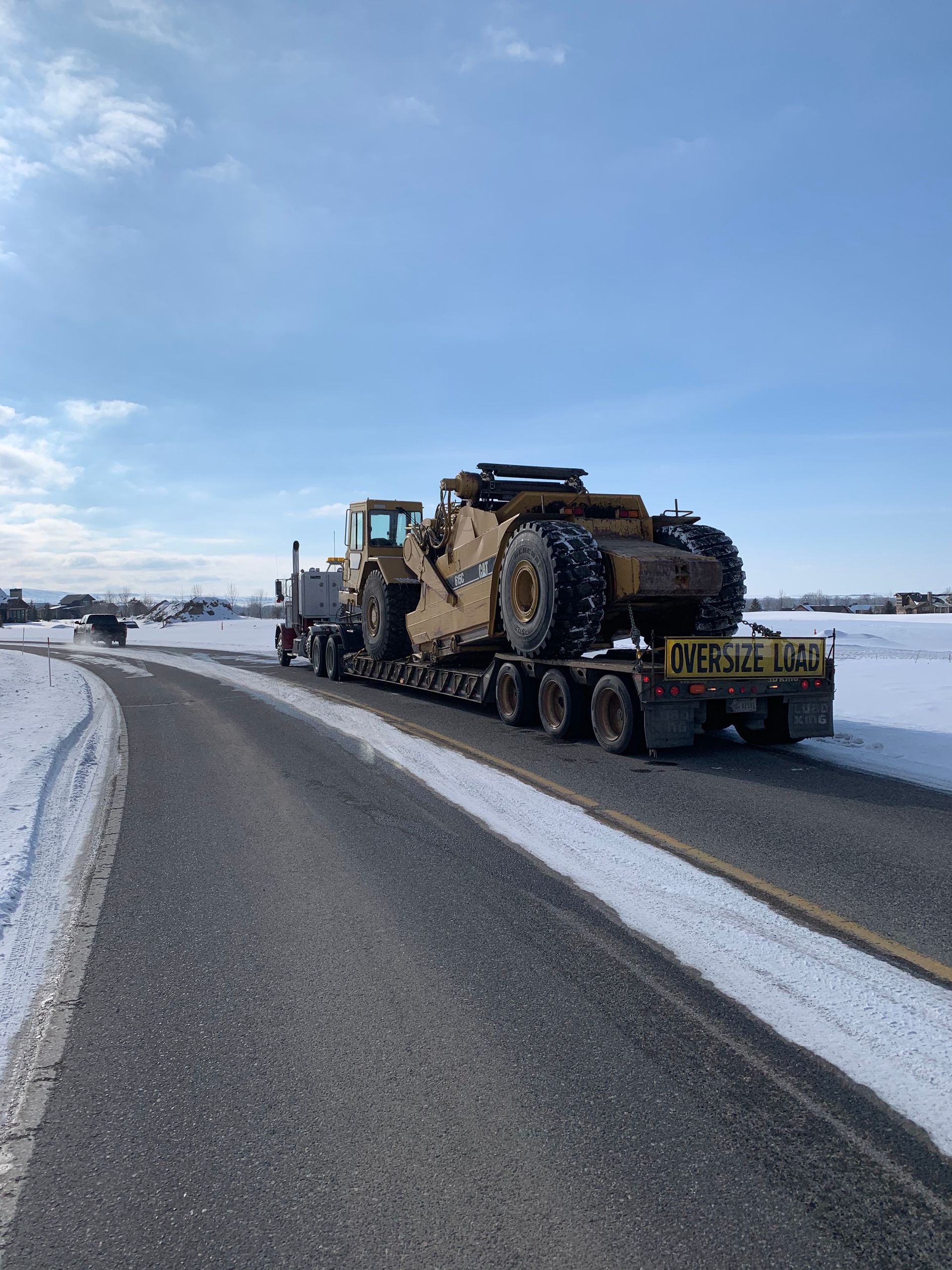 A truck is carrying a large bulldozer down a snowy road.
