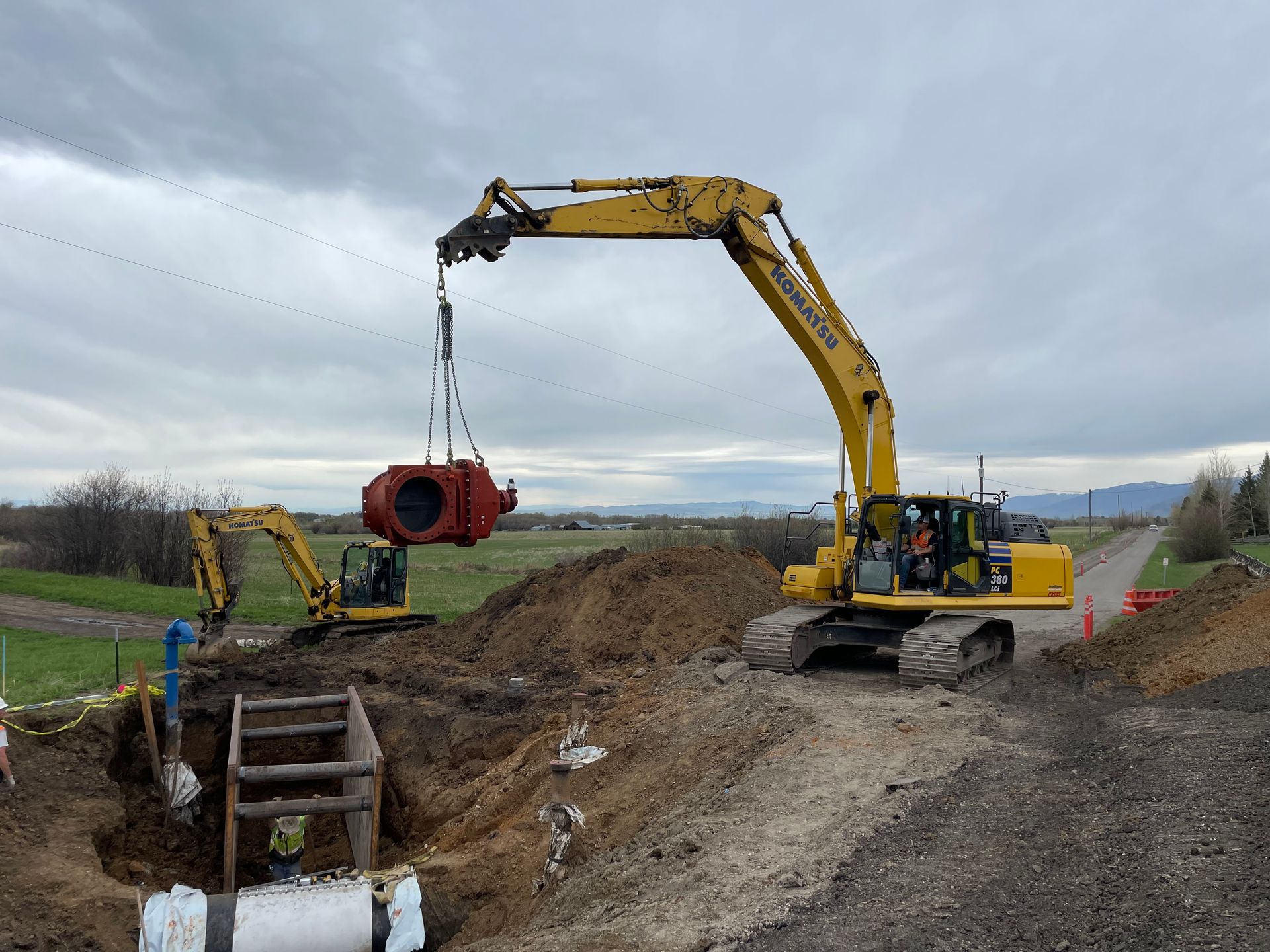A large yellow excavator is lifting a large red pipe out of the ground.