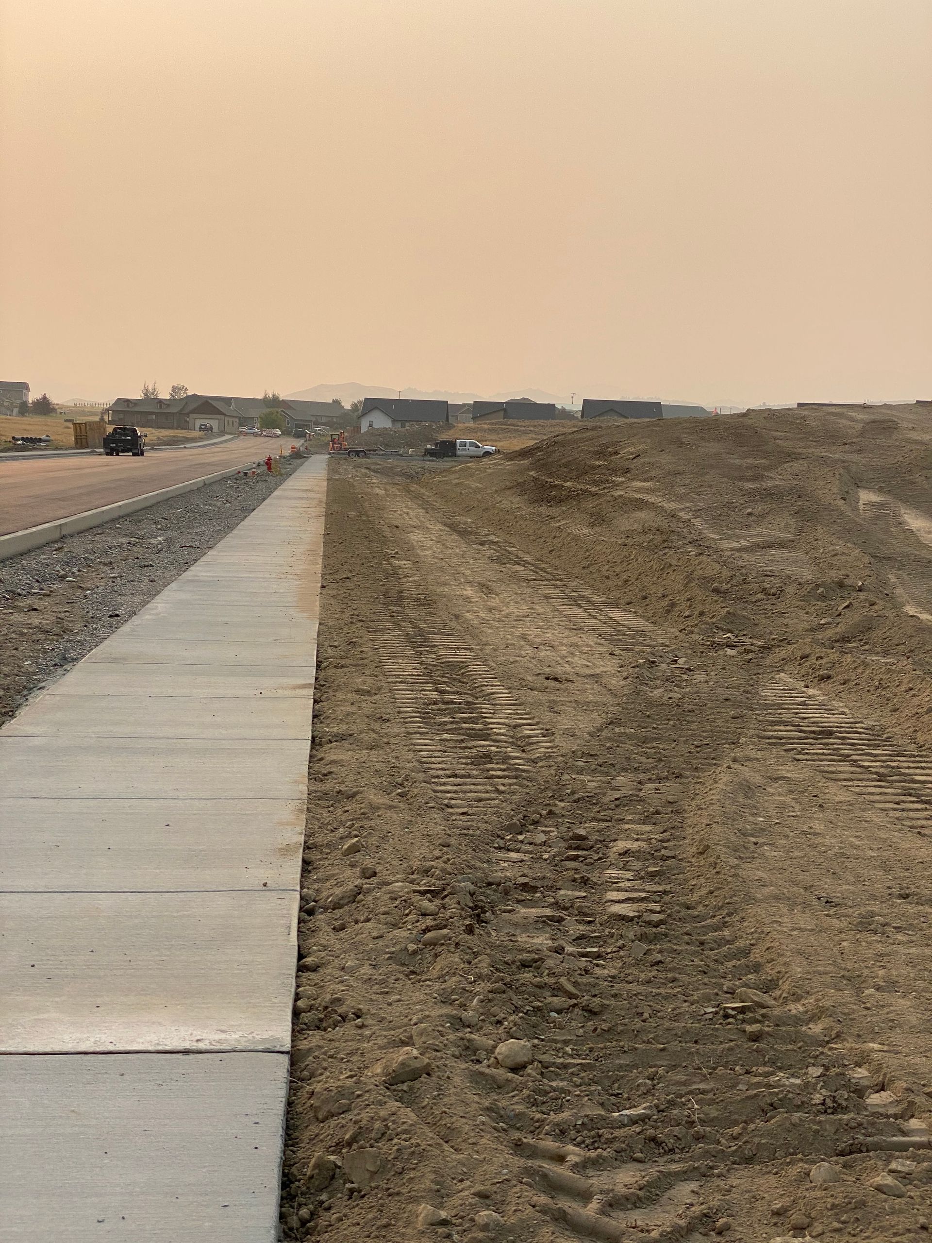 A sidewalk is going through a dirt field next to a road.