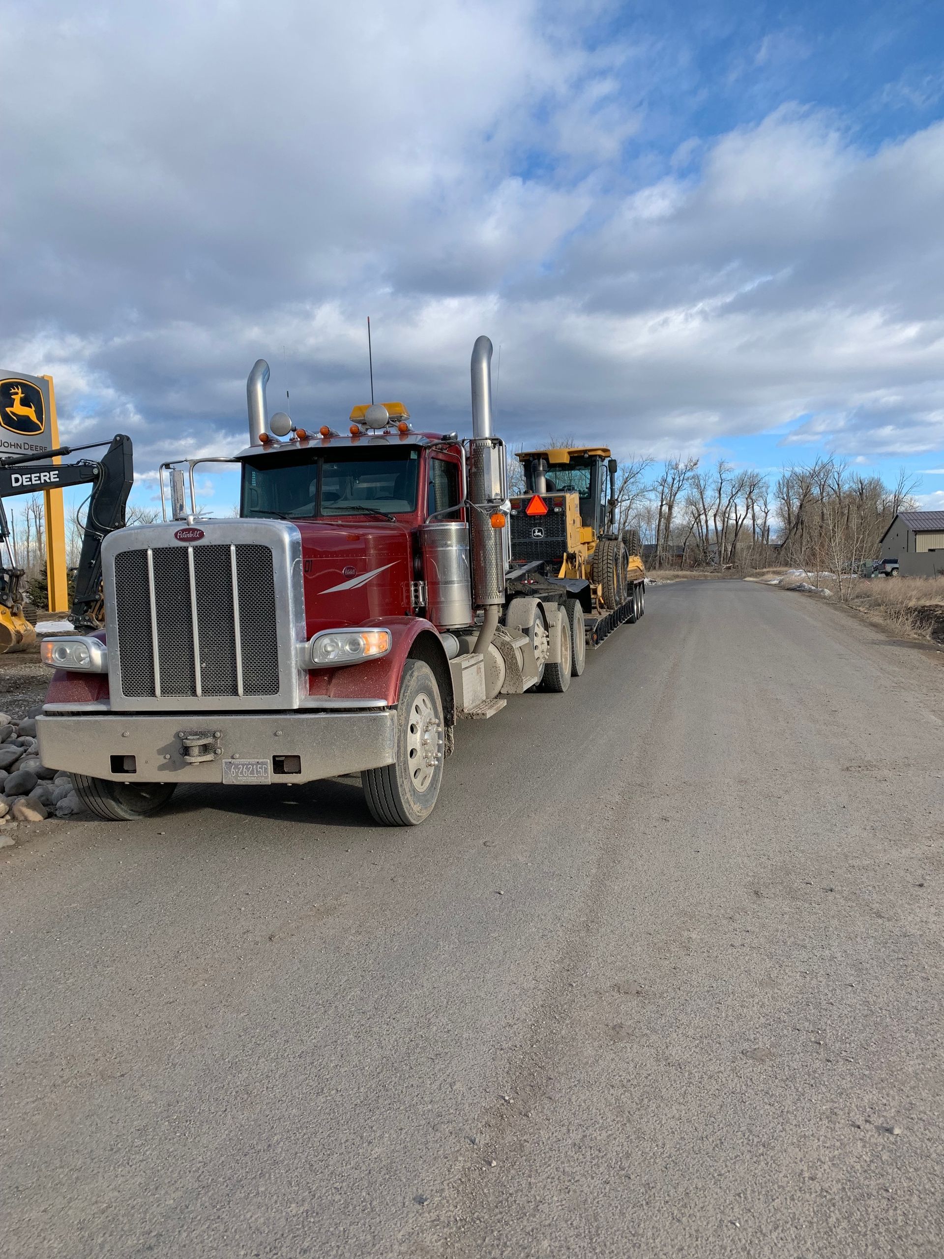 A red semi truck is parked on the side of the road next to a bulldozer.