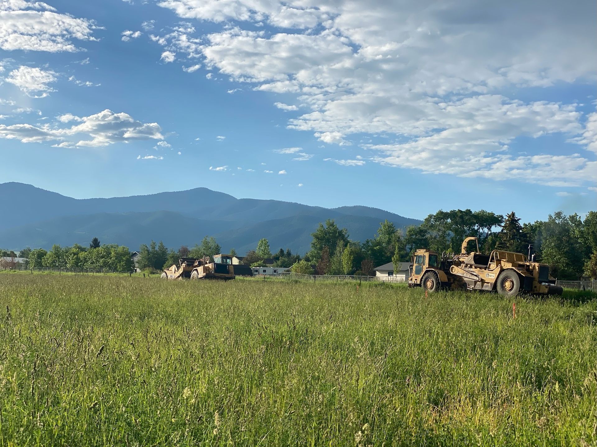 A bulldozer is driving through a grassy field with mountains in the background.