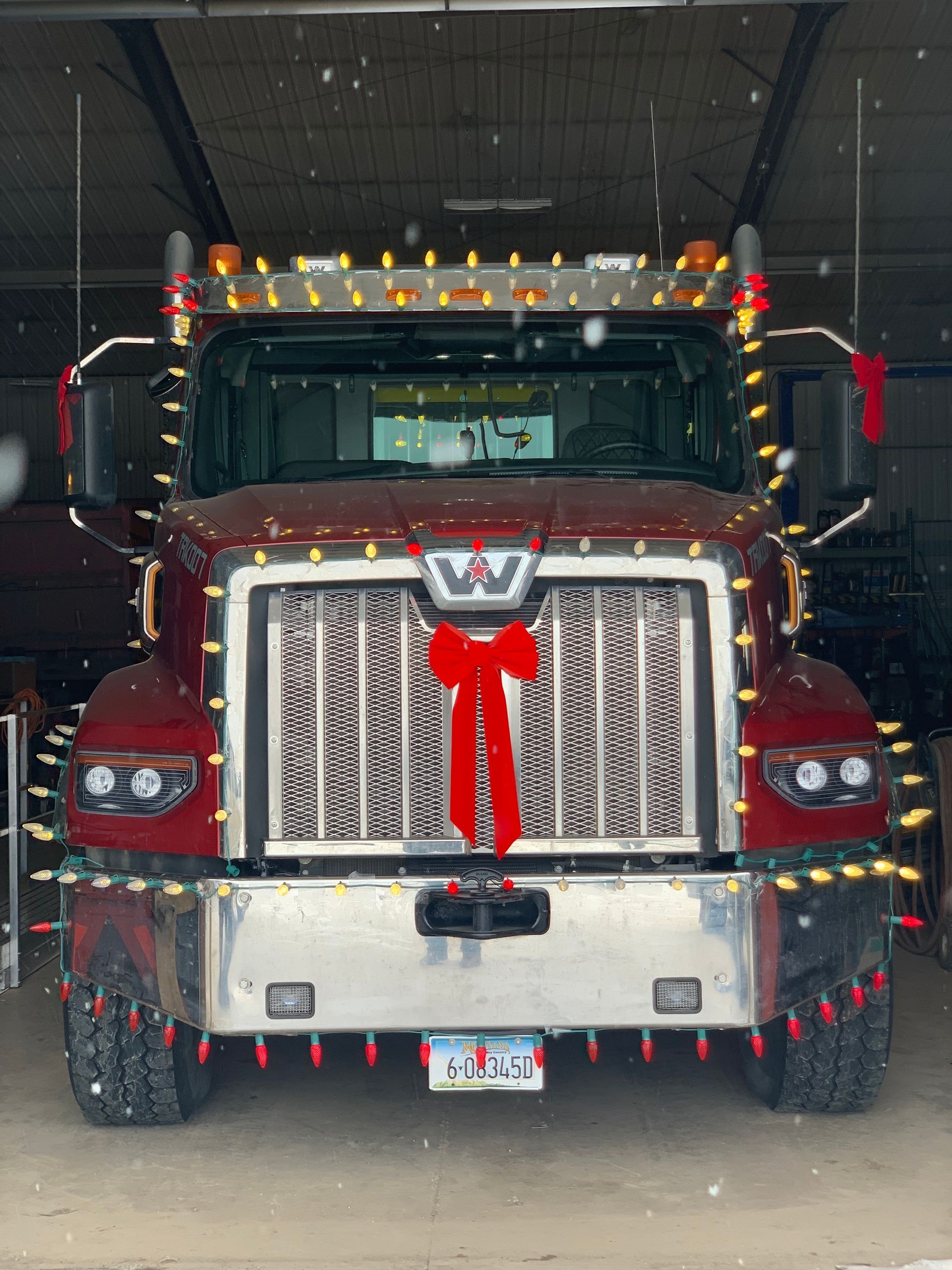 A red semi truck is decorated with christmas lights and a red bow.