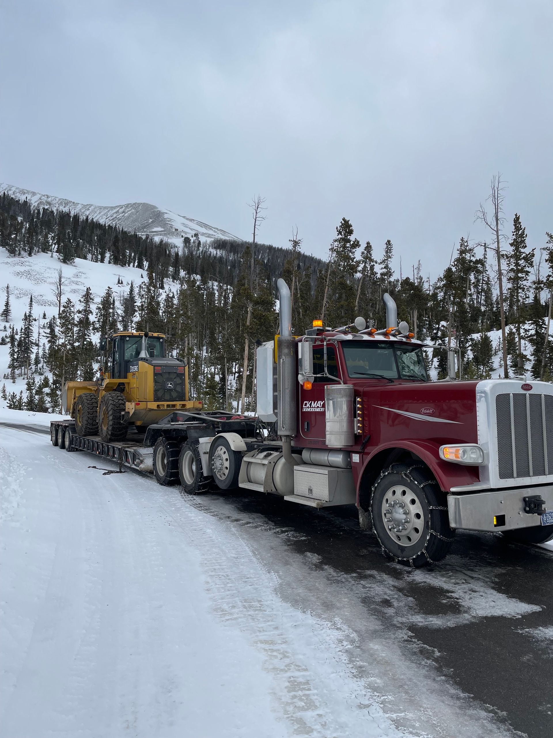 A semi truck is carrying a bulldozer down a snowy road.