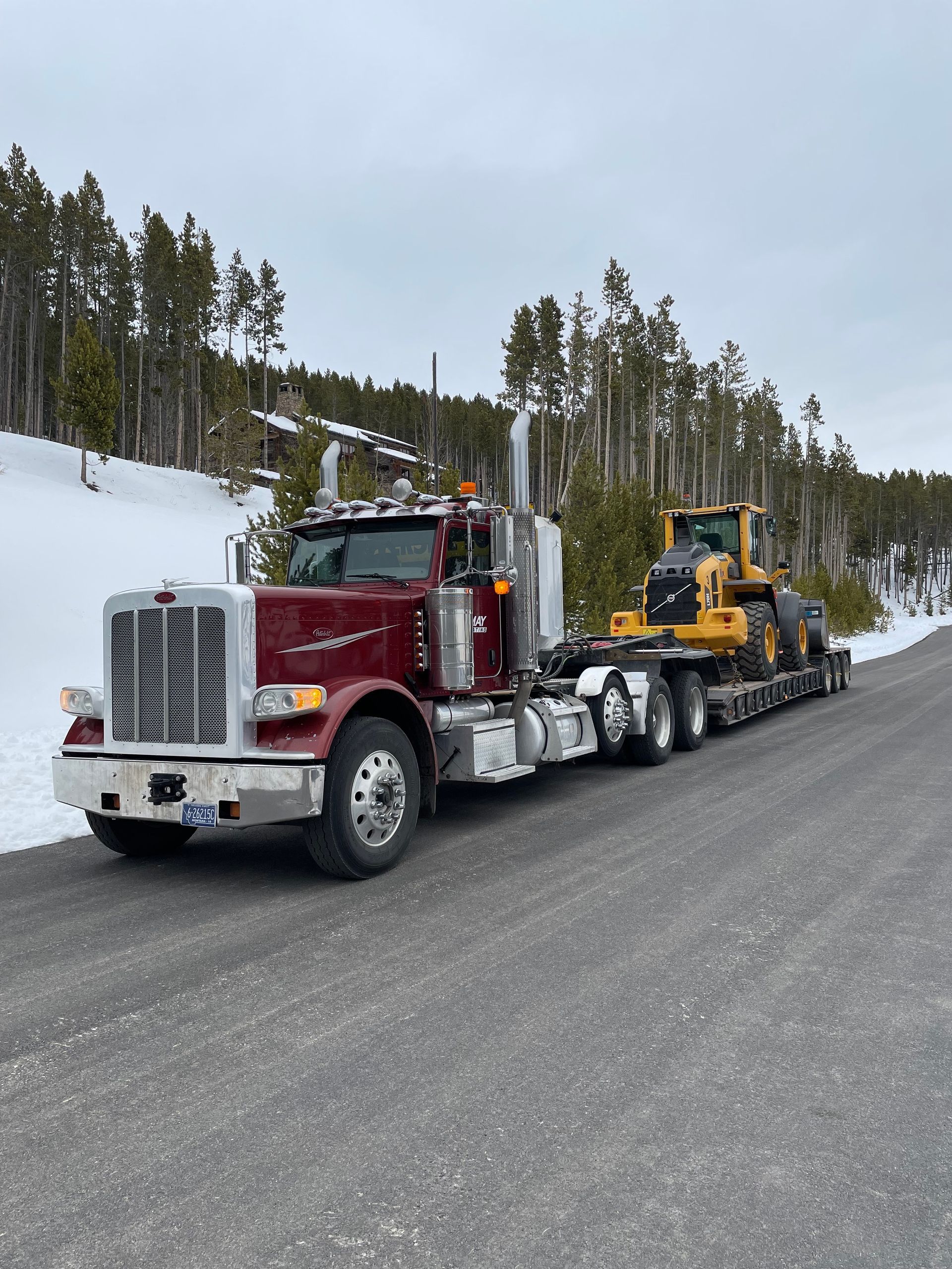 A semi truck is carrying a bulldozer down a snowy road.