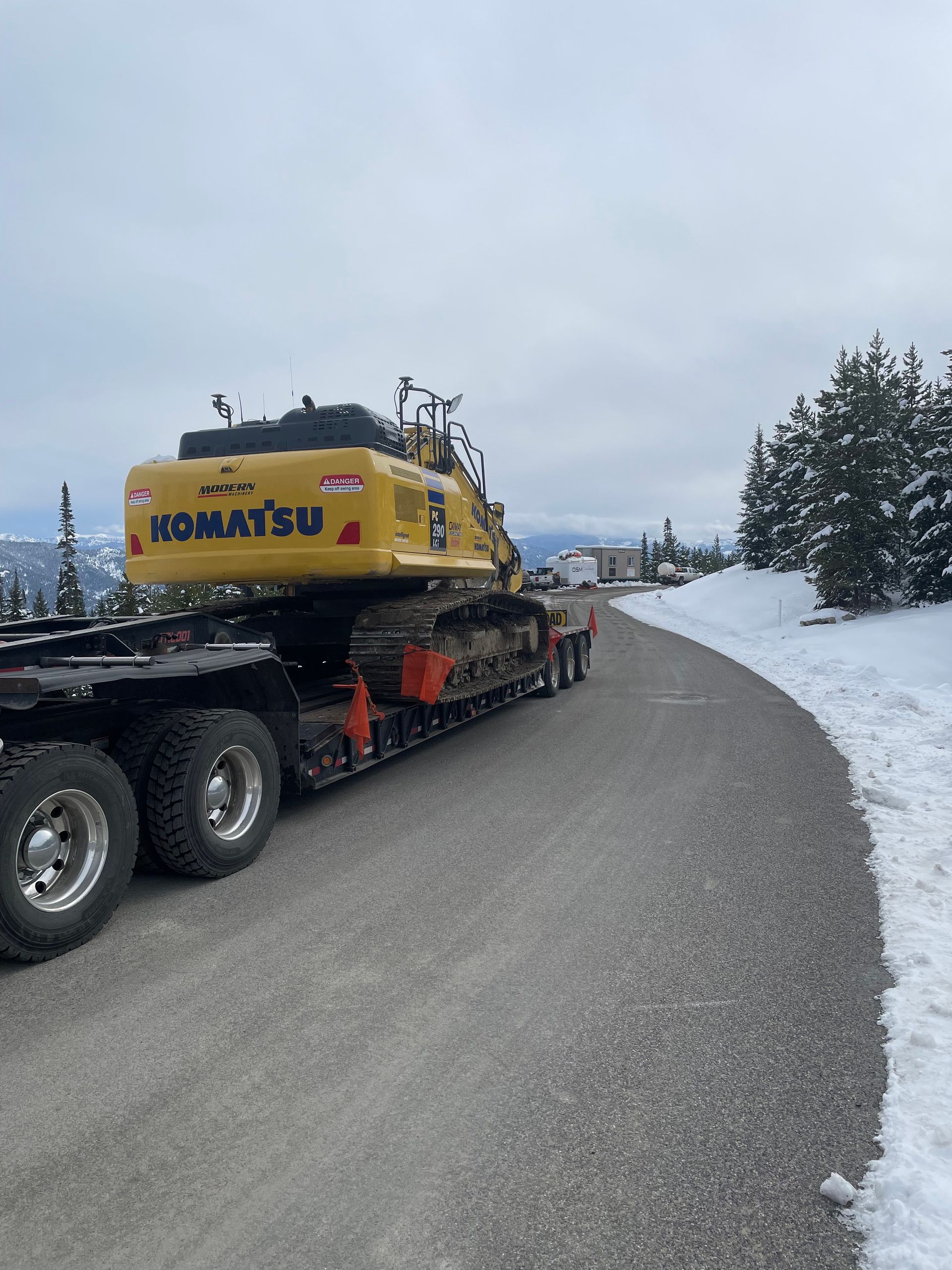 A komatsu excavator is being transported on a trailer on a snowy road.